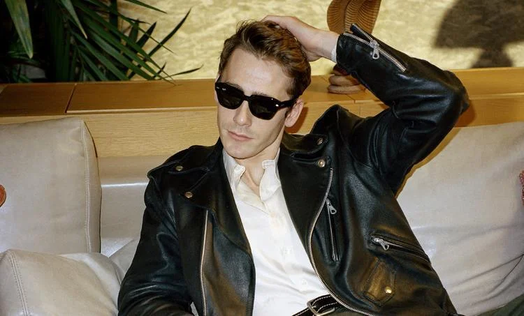 Person in a leather jacket and Ray-Ban RB0707S Sunglasses by Ray-Ban, sitting on a couch, and resting their hand on their head.