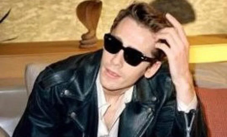 Person in a leather jacket and Ray-Ban BILL RB2198 Sunglasses, sitting down and stylishly touching their hair.